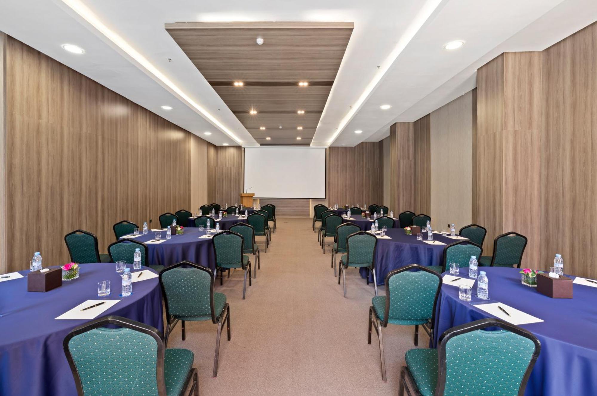 Savoy Le Grand Hotel Marrakech Marrakesh Exterior photo The photo shows an interior space set up for a conference or meeting. There are multiple round tables covered with dark blue tablecloths, and each table has green chairs arranged around it. On the tables, there are notepads, pens, and small water bot