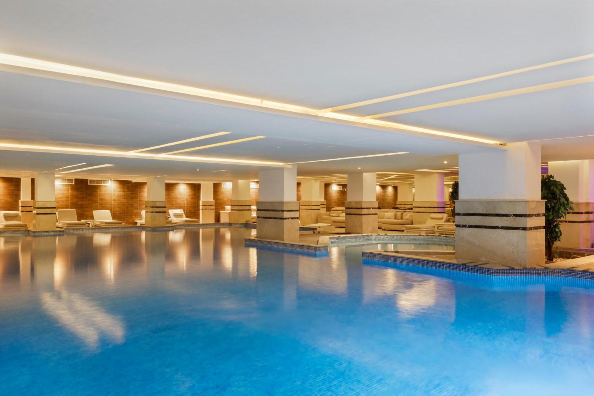Savoy Le Grand Hotel Marrakech Marrakesh Exterior photo The photo shows an indoor swimming pool area. The pool is filled with clear blue water, and the space is well-lit, with modern lighting fixtures along the ceiling. On the sides, there are lounge chairs arranged neatly. The walls have a light-colored 